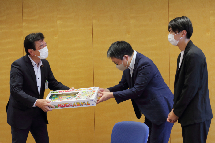 野々市市の粟市長（左）にBeyond SDGs人生ゲームを贈呈する平本所長（中央）