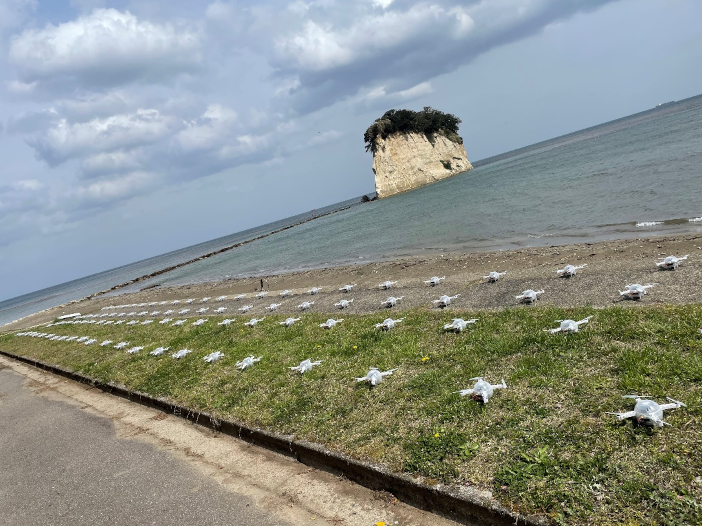 離陸準備中の100台のドローンと見附島