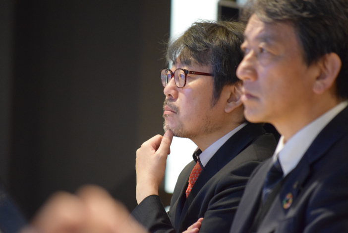 成果報告を聞き入る北菱電興の小倉一郎代表取締役社長（写真左）