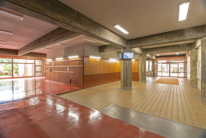 当時は左の掲示板の場所に下駄箱があった。現在も、土足エリアの名残として、タイル敷きが残っている(撮影:勝原基貴) 当時は左の掲示板の場所に下駄箱があった。<br>現在も、土足エリアの名残として、タイル敷きが残っている(撮影:勝原基貴)