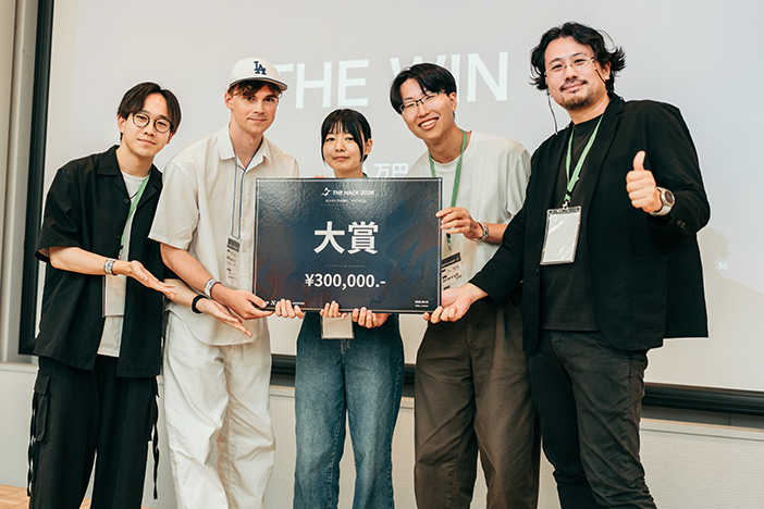 大賞を受賞した学生チーム「THE WIN」。<br>写真左から久米蒼輝さん(情報工学科4年)、マルチェンコ・ダニールさん(情報工学科4年)、松本絆那さん(情報工学科3年)、高岡 己太朗さん(情報工学科3年)、審査員でなるセミ代表・成瀬允宣さん<br> ※出典:X(@thehack_pj) 大賞を受賞した学生チーム「THE WIN」。<br>写真左から久米蒼輝さん(情報工学科4年)、マルチェンコ・ダニールさん(情報工学科4年)、松本絆那さん(情報工学科3年)、高岡 己太朗さん(情報工学科3年)、審査員でなるセミ代表・成瀬允宣さん<br> ※出典:X(<a href="https://x.com/thehack_pj" target="_blank">@thehack_pj</a>)