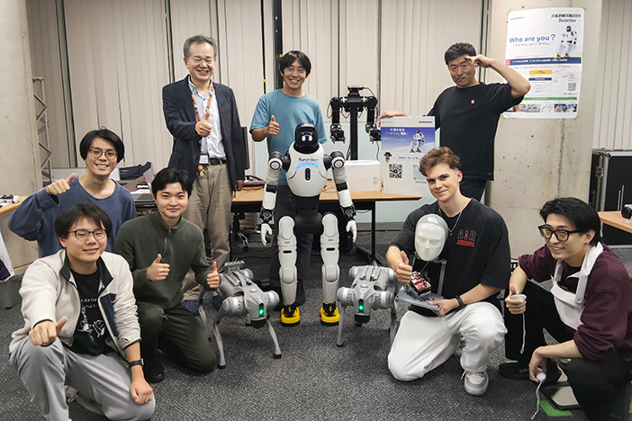 開発には新たなコーオプ教育モデルが採用され、<br>企業技術者の指導を受けながら、研究室にいながらにして学生により開発が進められた。<br><b>［教員・企業技術者および学生開発メンバー］</b><br>上段左より、中沢実(金沢工業大学)、折池雄太(AIロボットシステムズ)、小林康博(金沢機工)<br> 下段左より、並川天夢(学部/メディア情報学科 4年)、田和広大(大学院/情報工学専攻2年)、<br class="hidden-sp"> 鷲尾太乙(大学院/電気電子工学専攻1年)、マルチェンコダニール(学部/情報工学科4年)、松田彩成(学部/情報工学科4年)
